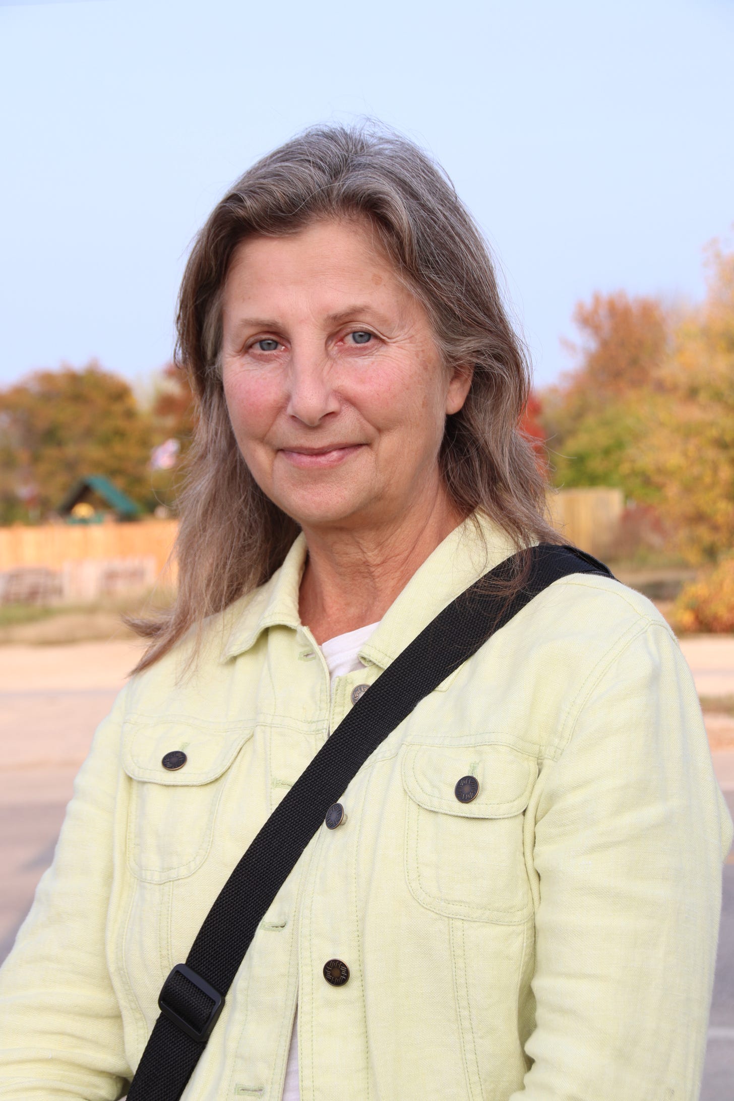 Tangi Bell stands outside under a blue sky, wearing a pale yellow jacket. Tangi Bell stands outside under a blue sky, wearing a pale yellow jacket.