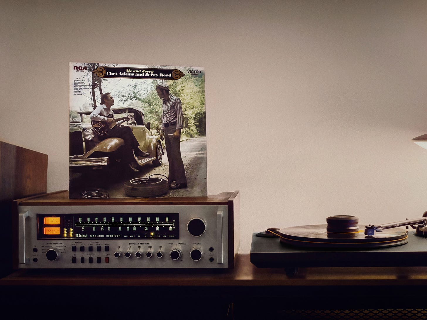 Me and Jerry by Chet Atkins and Jerry Reed (RCA Victor, 1970), the LP sleeve standing upright on a wood-cased McIntosh MAC 4100 receiver with its tuning dial lit amber. On the cover, Atkins and Reed on a tree-lined country road beside an antique car — one seated on the fender with a guitar, the other standing in a striped shirt, bell-bottoms, and a hat. Color photograph by Sean Perry for The Sunday Find.
