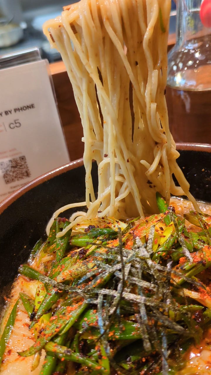 Shoyu Truffle Ramen bowl with pork chashu, and Spicy Negi Tonkotsu ramen with noodles being pulled up.