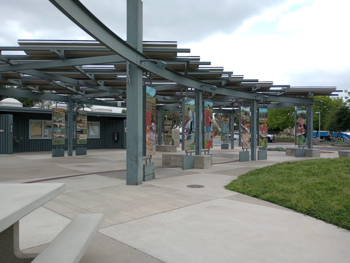 Gazebo stucture made of girders, with colorful graphic panels attached, and restrooms behind
