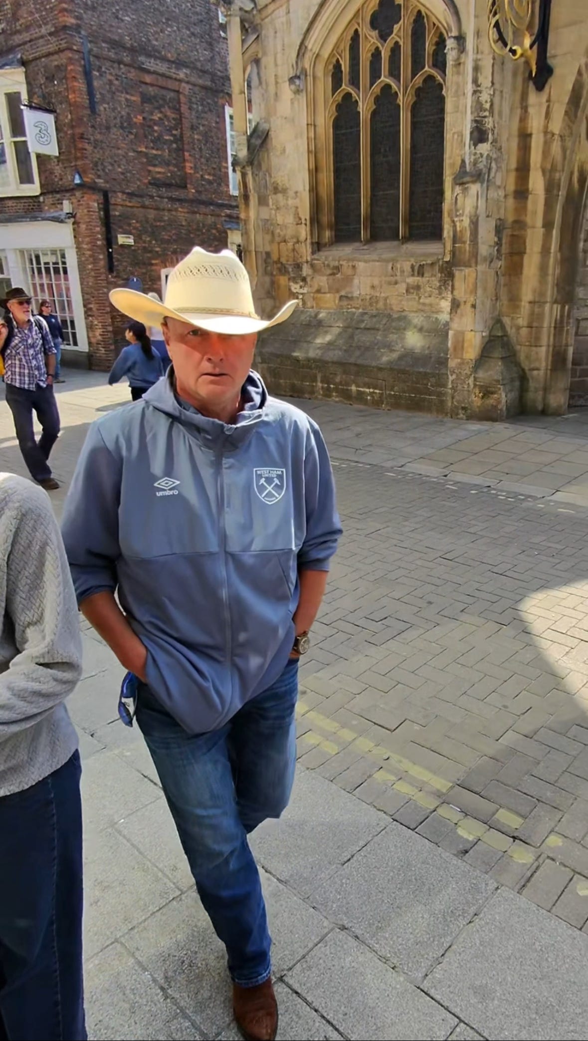 A man in a West Ham jacket, cowboy hat and boots, approaches the camera