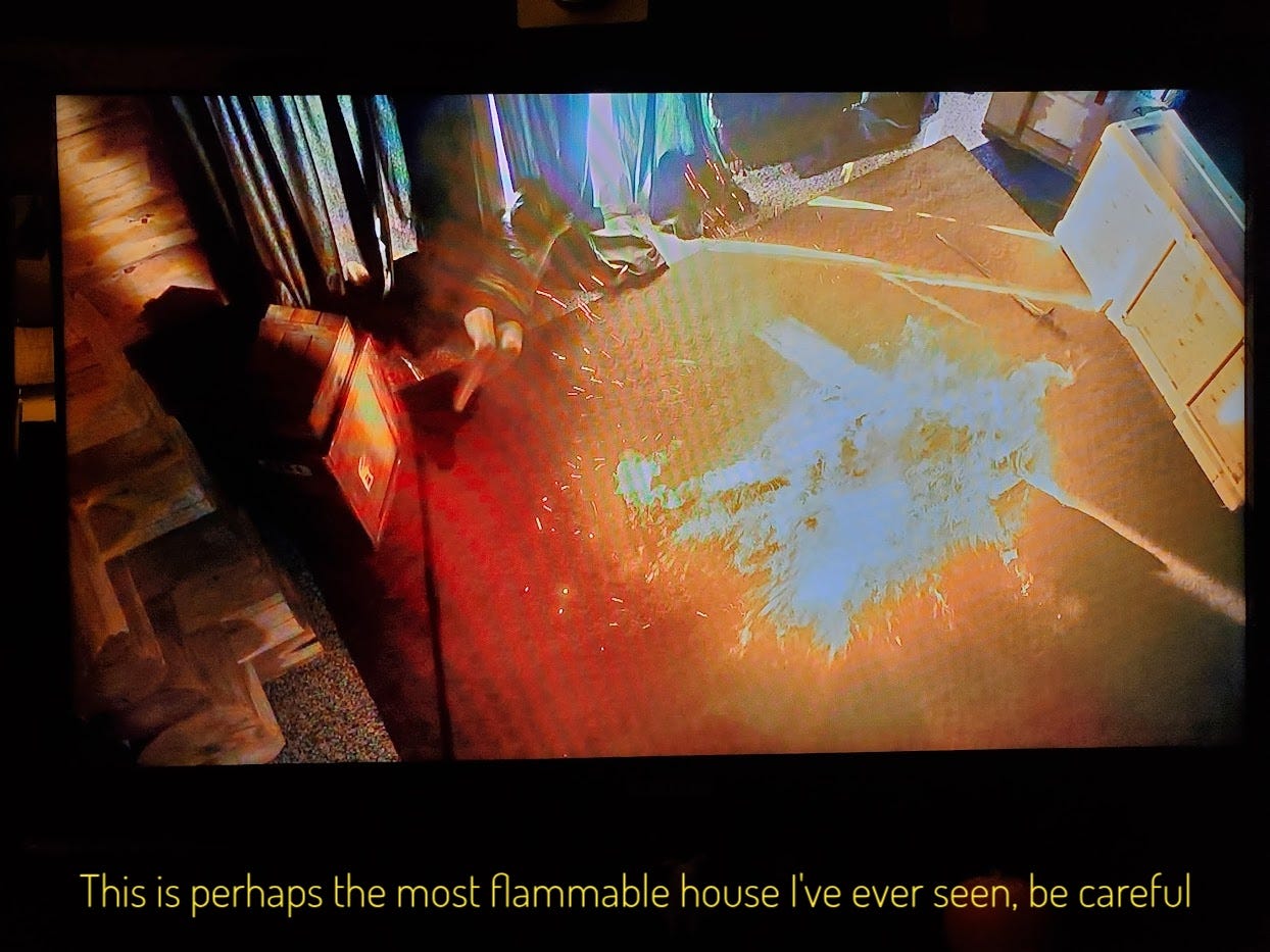 A Cole-shaped thing burning on the floor of a log house, captioned "This is perhaps the most flammable house I've ever seen, be careful"
