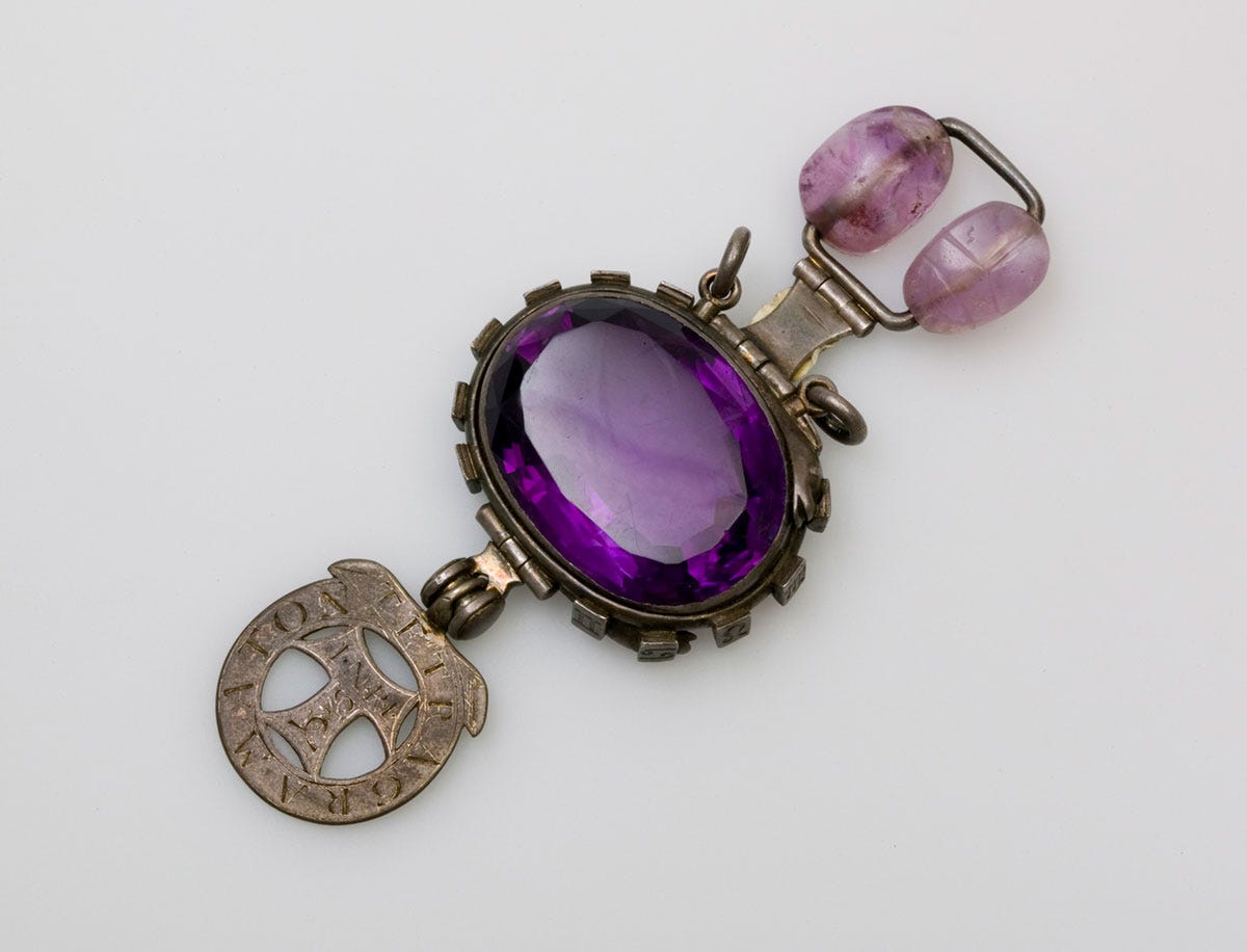 A large purple gemstone set in silver, with another purple stone and silver medallion attached to either side