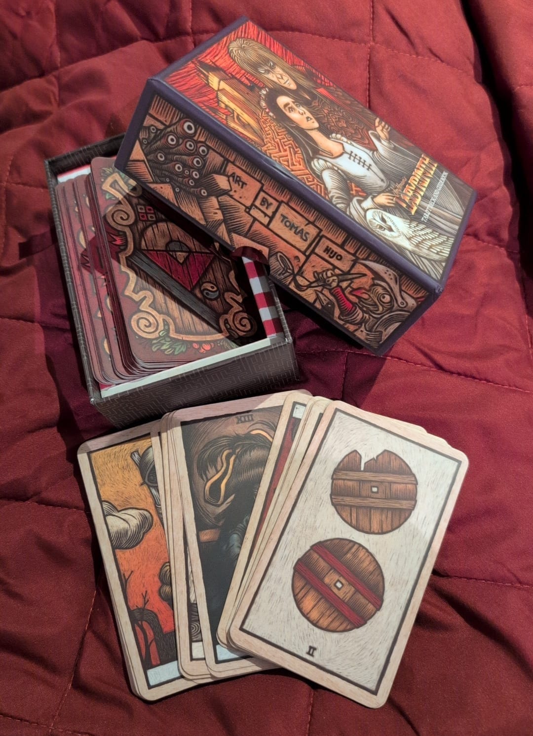 Open Labyrinth Tarot box on a burgundy quilt with several cards spread out beside it, revealing the Tomas Hijo artwork and deck design. Behind-the-scenes image from Amy Twigg’s Tarot DMs interview, highlighting her favourite tarot deck and visual influences. Open Labyrinth Tarot box on a burgundy quilt with several cards spread out beside it, revealing the Tomas Hijo artwork and deck design. Behind-the-scenes image from Amy Twigg’s Tarot DMs interview, highlighting her favourite tarot deck and visual influences.