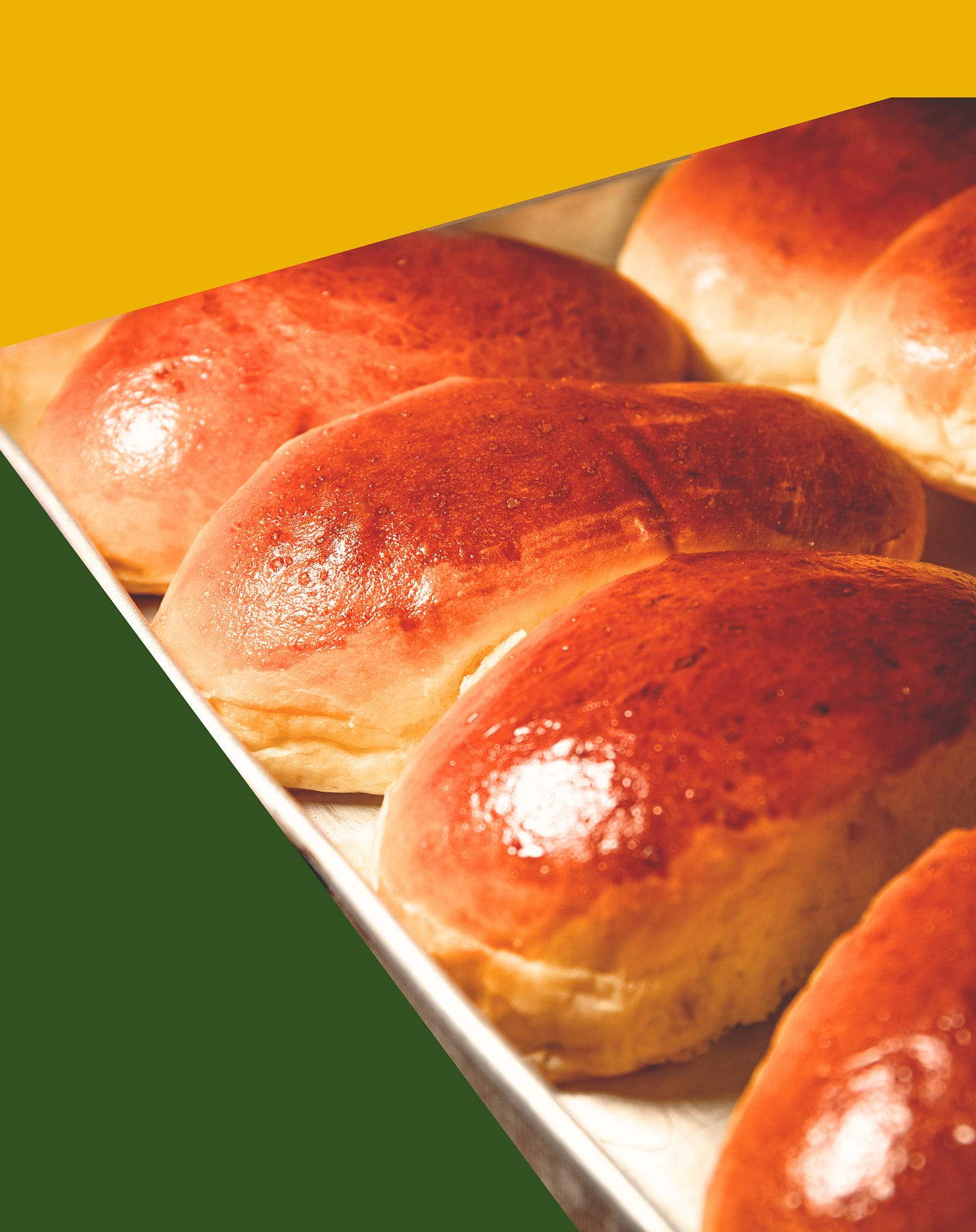oval bread rolls, golden brown exterior, on baking tray with golden yellow triangle and green triangles around the edge.