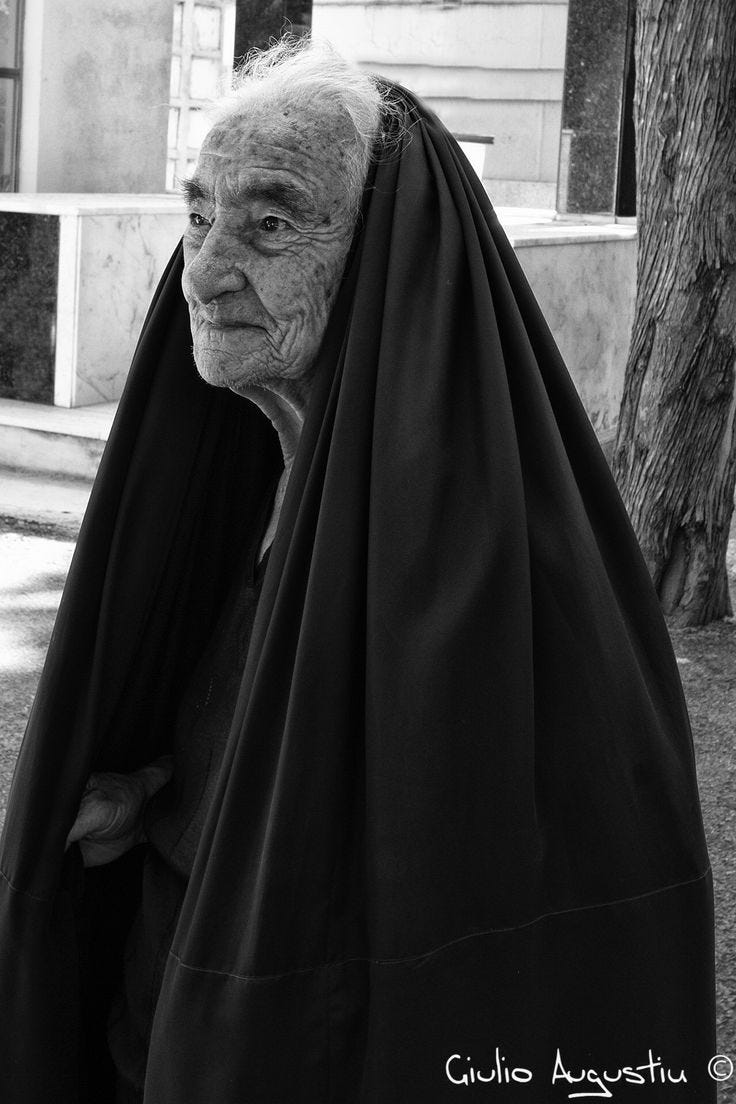 This may contain: an old woman with a black cloak on her head
