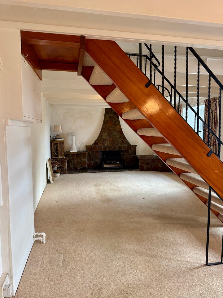 An old fashioned fireplace that took up a whole back wall with dark stone, with built in shelving units and a surround above the fire going up to the ceiling. 