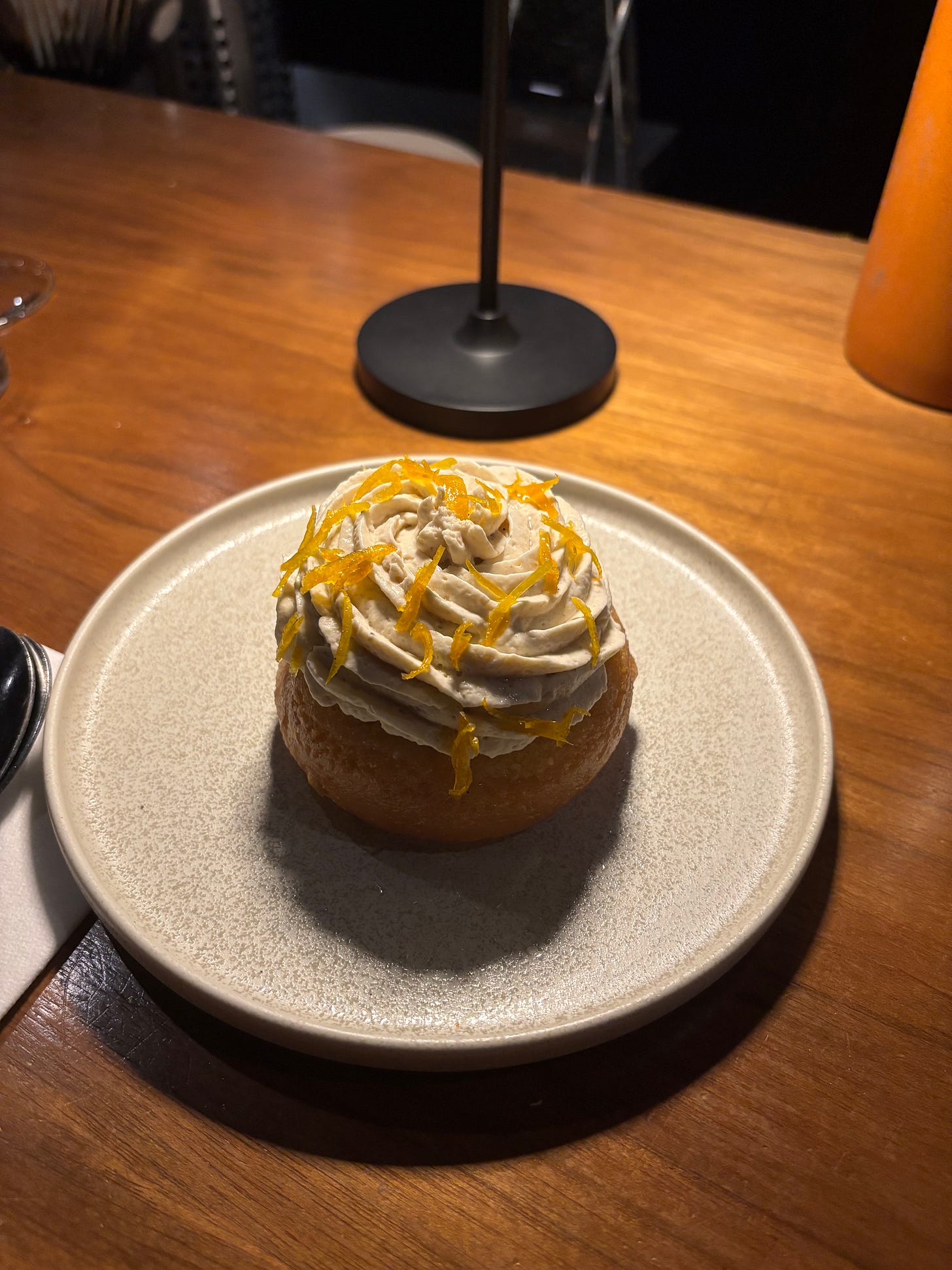 A stoneware plate with a round dessert on it, topped with cream and orange zest.