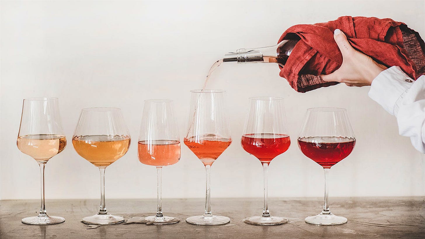 A lineup of glasses of rosé in different shades, from pale pink to light red, with a bottle being poured into one glass A lineup of glasses of rosé in different shades, from pale pink to light red, with a bottle being poured into one glass