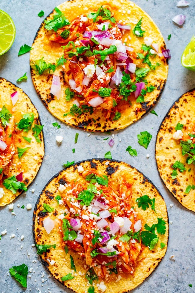 two Chicken Tinga Tacos topped with cilantro, tomato, onions, and lime. 