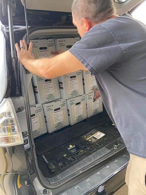 A box filled with white eggplant with a sign taped on it with information about the produce. A man loading boxes of produce in a van. A stack of boxes sitting on top of a pallet.