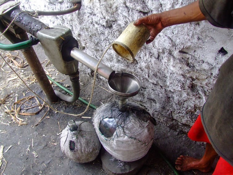 Hand of man holding cup over metal contraption made up of tubes and funnels. Hand of man holding cup over metal contraption made up of tubes and funnels.