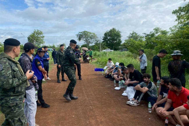 Les migrants arrêtés, assis par terre, visage baissé, devant un groupe de rangers thaÏlandais. Les migrants arrêtés, assis par terre, visage baissé, devant un groupe de rangers thaÏlandais.