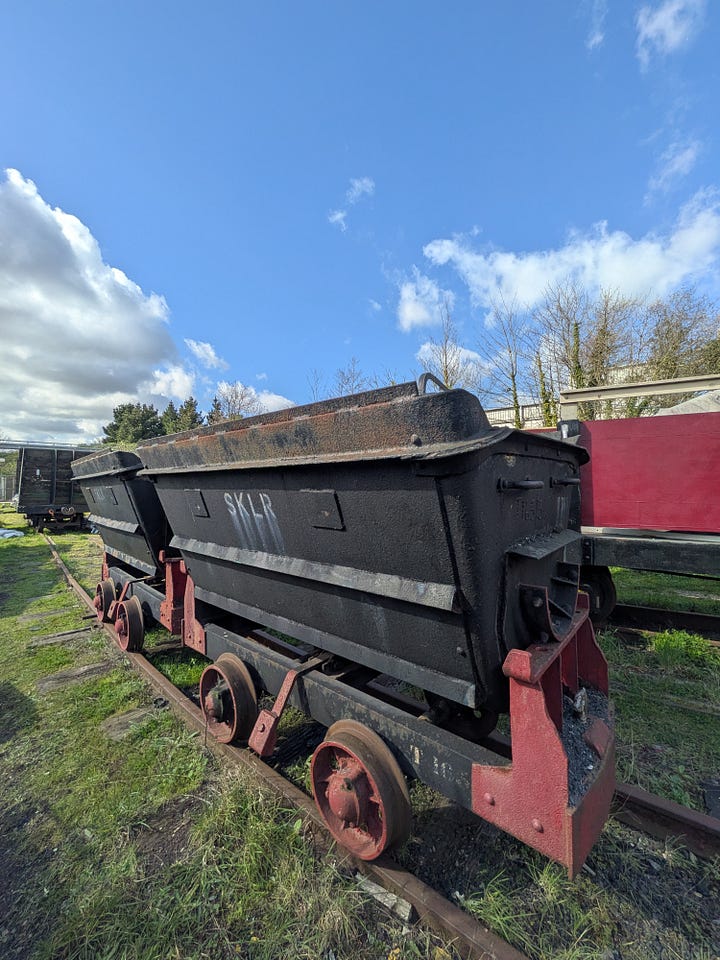 A small green steam train and some wagons, with blue sky