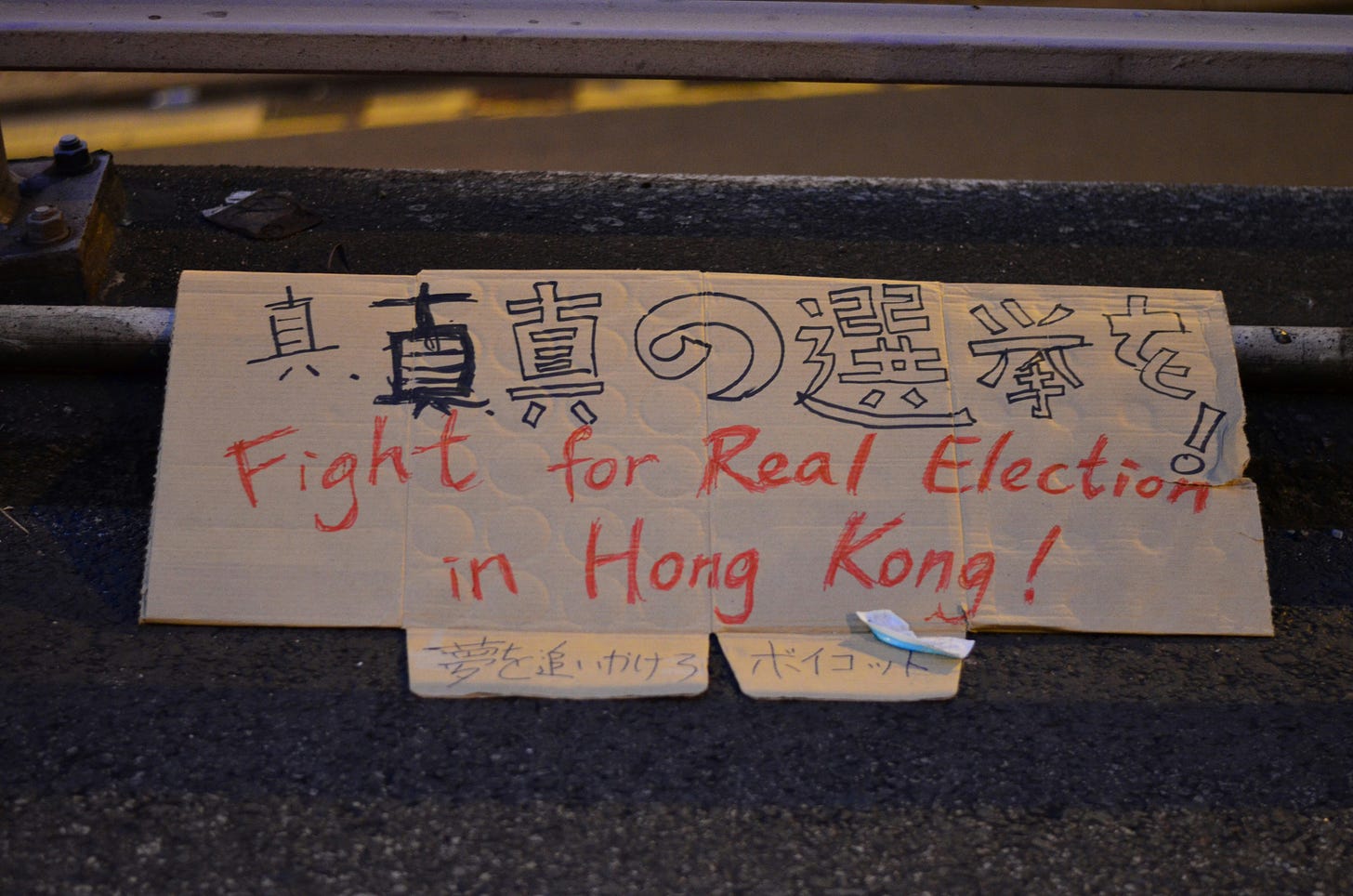Placa escrita em mandarim e em inglês com a mensagem de lute por eleições democráticas em Hong Kong