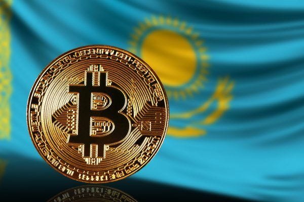 A golden Bitcoin coin with the Bitcoin symbol engraved on it is placed in front of a blue flag featuring a yellow sun and eagle emblem representing Kazakhstan. A golden Bitcoin coin with the Bitcoin symbol engraved on it is placed in front of a blue flag featuring a yellow sun and eagle emblem representing Kazakhstan.