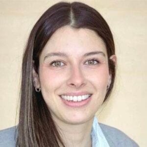 Foto de rosto de mulher branca de cabelos lisos castanhos compridos e olhos claros. Sorri para a foto