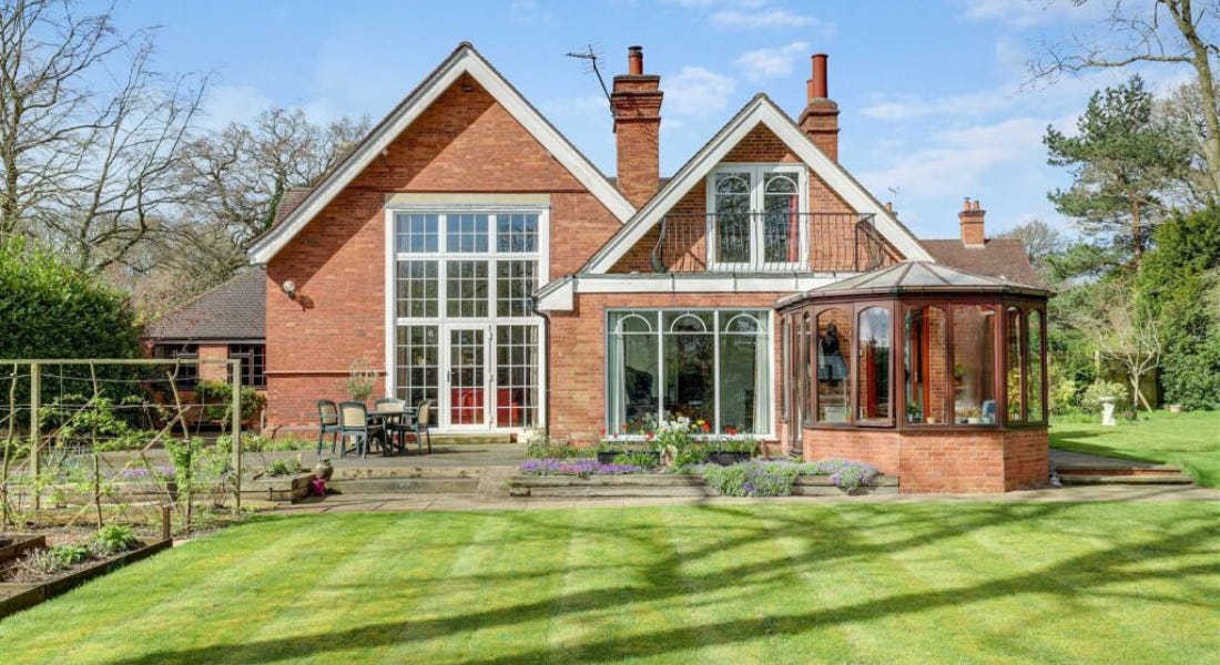 A brick house with two triangular roofs and large windows, with a green lawn and vegetable patch in front of it