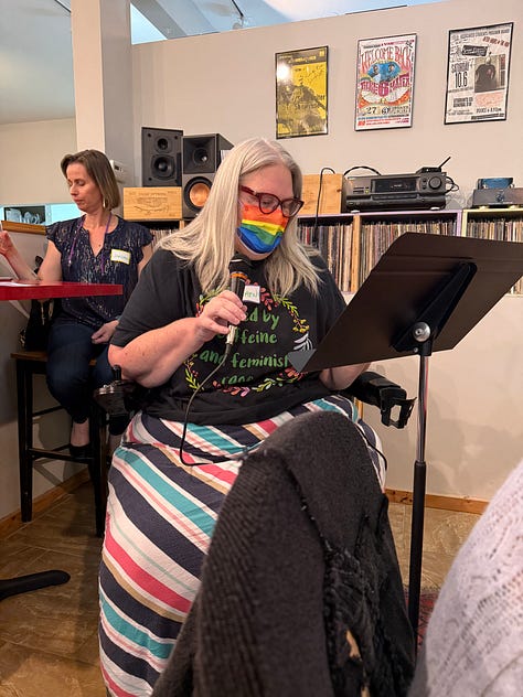 A group of people reading at an open mic inside a small wine bar.