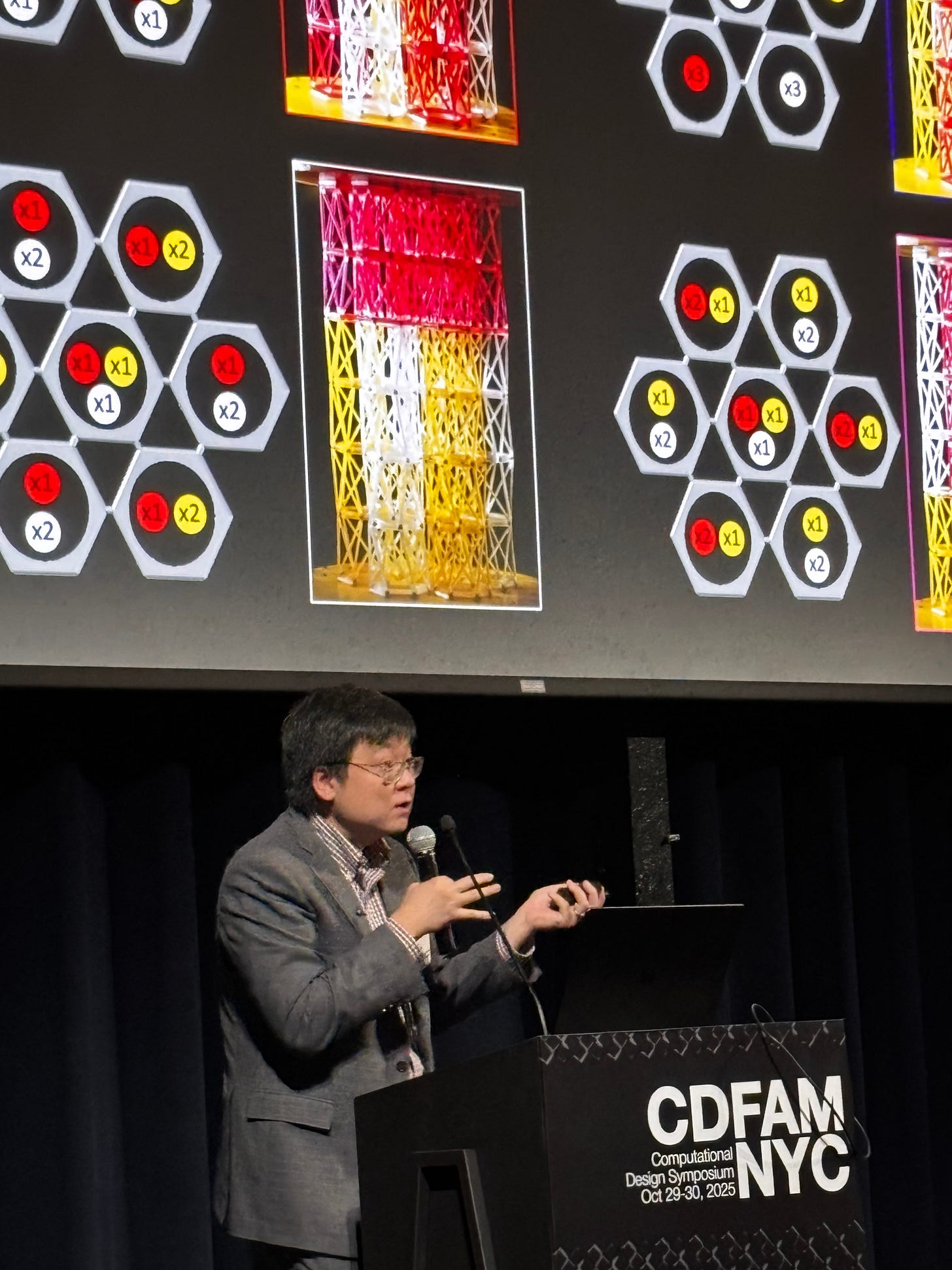 Tuo Zhao of Princeton presenting at the CDFAM NYC 2025 event, with a background display showing graphical representations of computational design elements in red, white, and yellow colors.