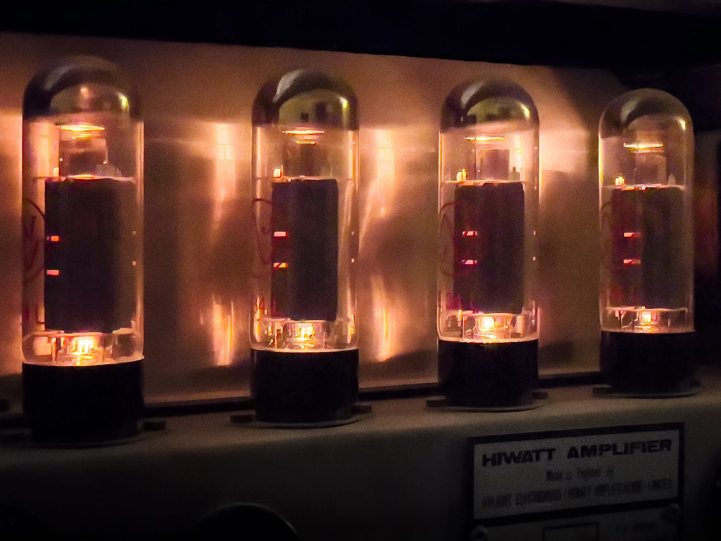 Four EL34 power valves glowing inside a Hiwatt amplifier, photographed from just above the chassis. Red lettering on the glass; the maker's plate reads Hiwatt Amplifier, made in England by Hylight Electronics. Warm heater light reflected in the steel. Color photograph by Sean Perry for The Sunday Find.