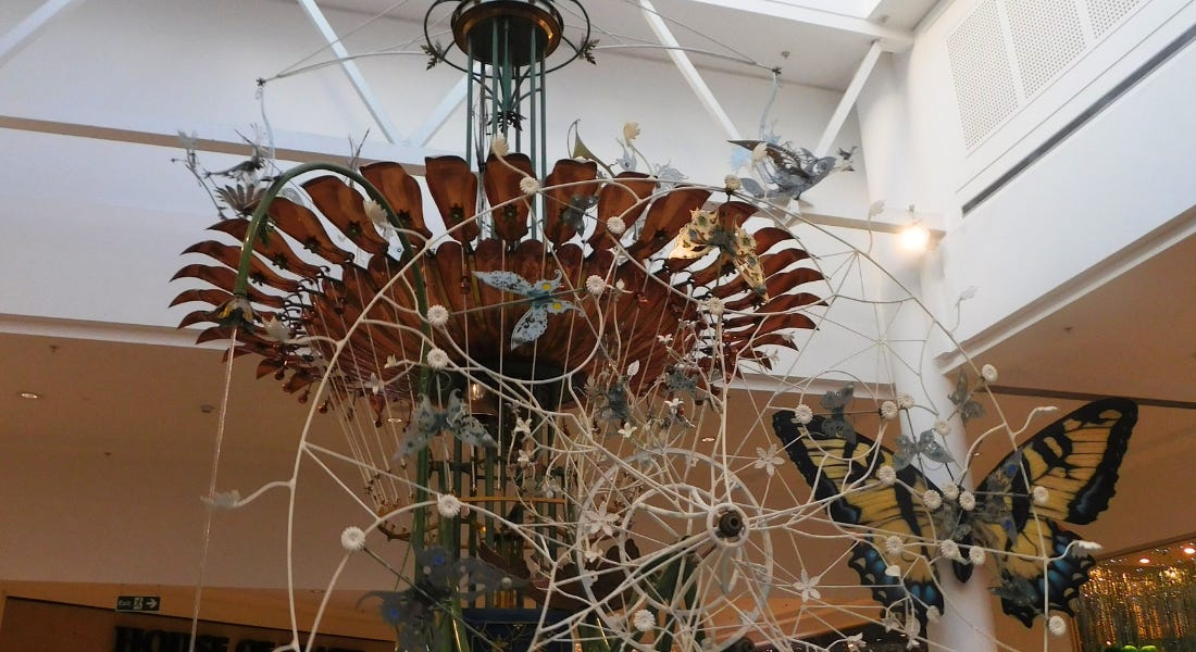 A tall clock structure with a copper flower and a white iron clock, with a white ceiling above it