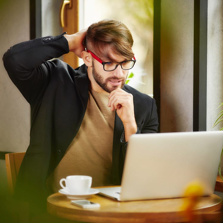 Man in coffee shop with laptop scratching his head.