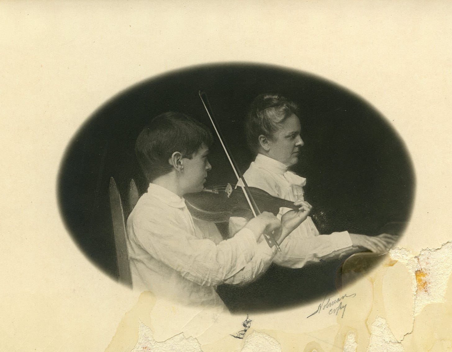 Woman seated at piano while young boy sits beside her playing violin.
