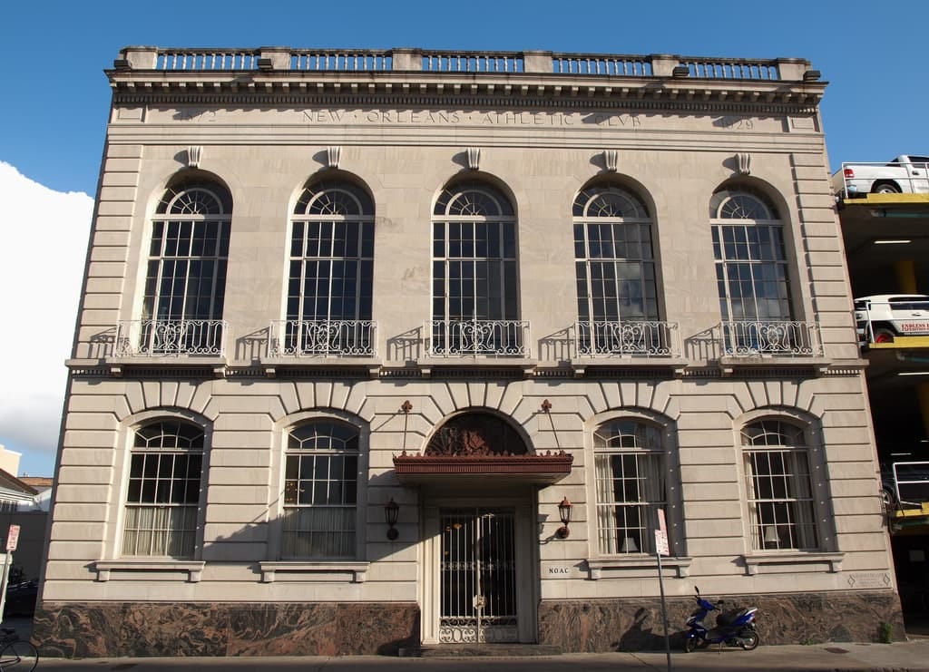 New Orleans Athletic Club’s facade. Two-story, white stone structure with a flat roof. The facade has arched windows and a central arched doorway.