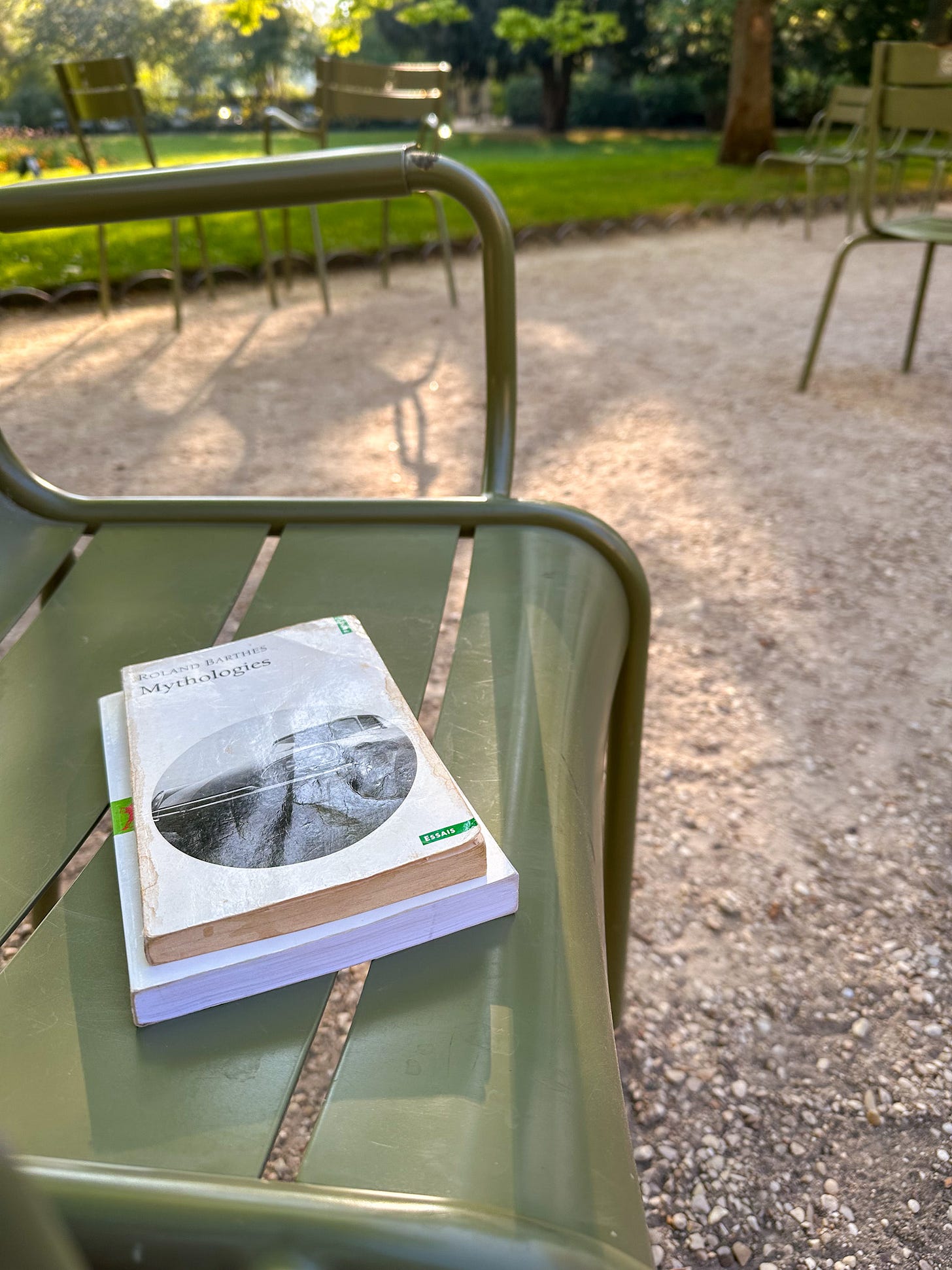 Close-up of two French books — "Mythologies" by Roland Barthes and "Victimes de la mode?" by Guillaume Erner — resting on a classic green Jardin du Luxembourg chair in Paris. Close-up of two French books — "Mythologies" by Roland Barthes and "Victimes de la mode?" by Guillaume Erner — resting on a classic green Jardin du Luxembourg chair in Paris.