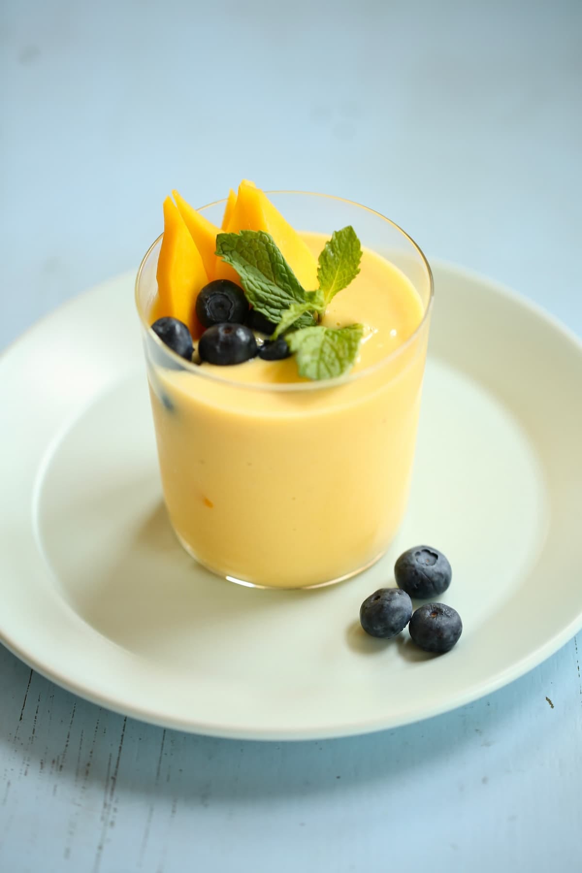 a side photo of a mango smoothie with blueberry garnish. 