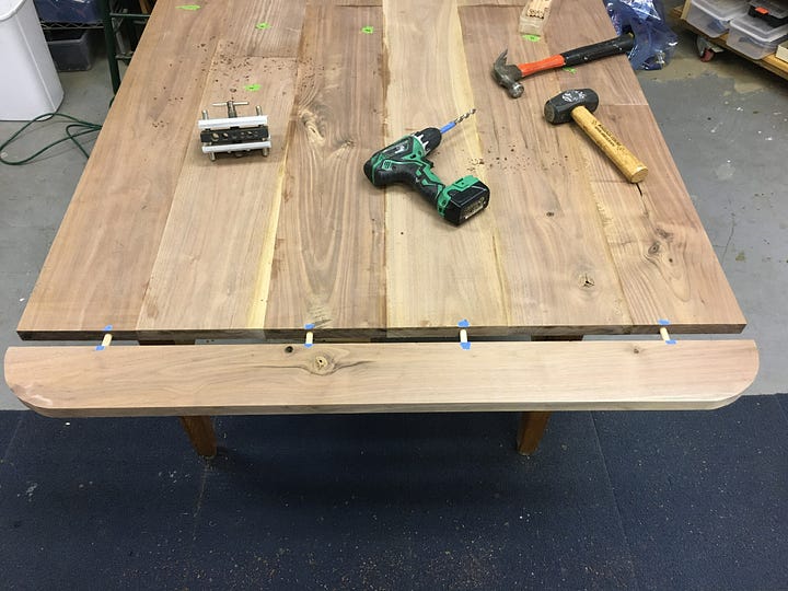boards lying on garage floor, boards cut and arranged into a tabletop, end piece with dowels, finished and painted