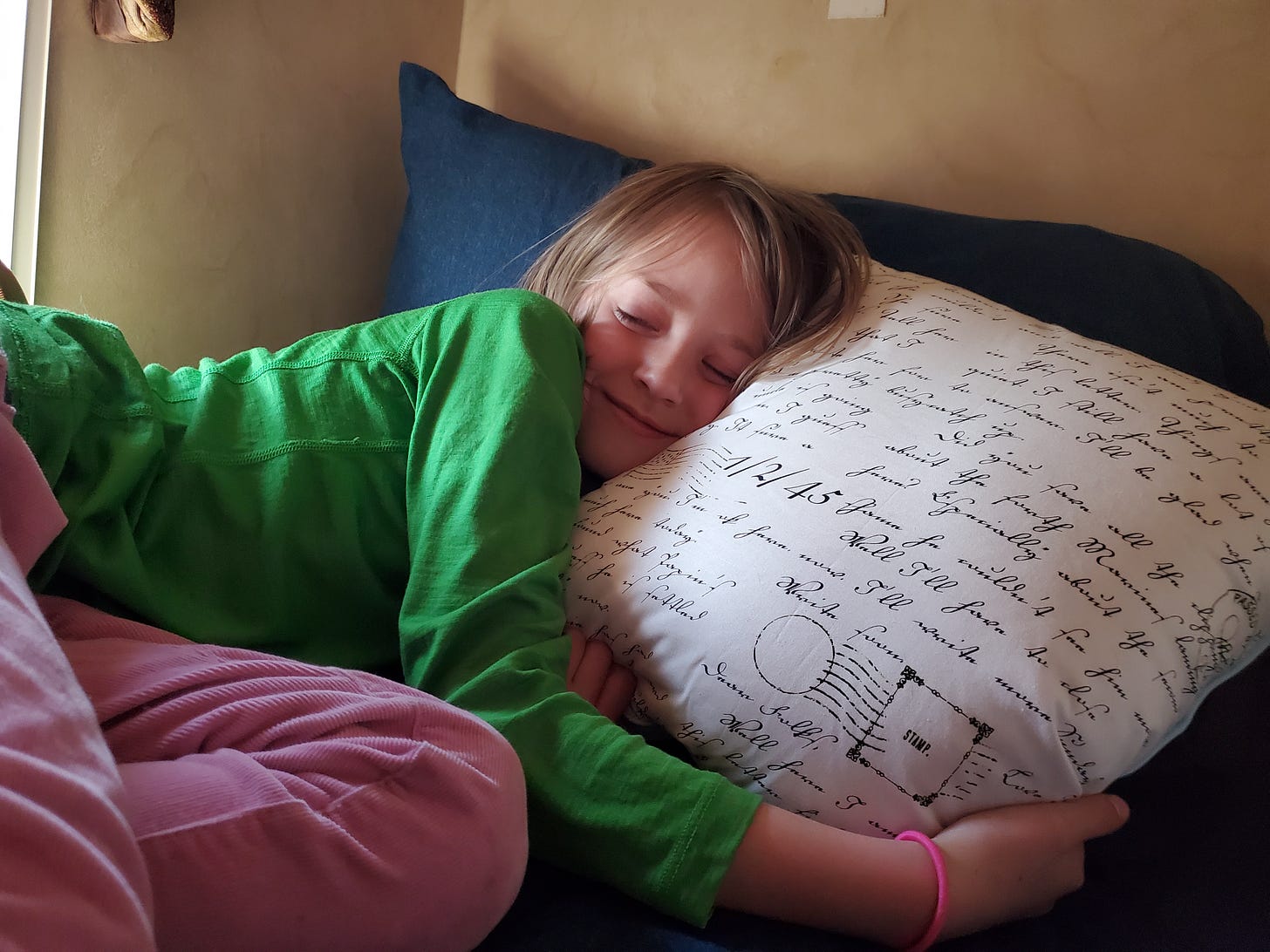 L smiling with her eyes closed and her head pressed against a white pillow in the top bunk.
