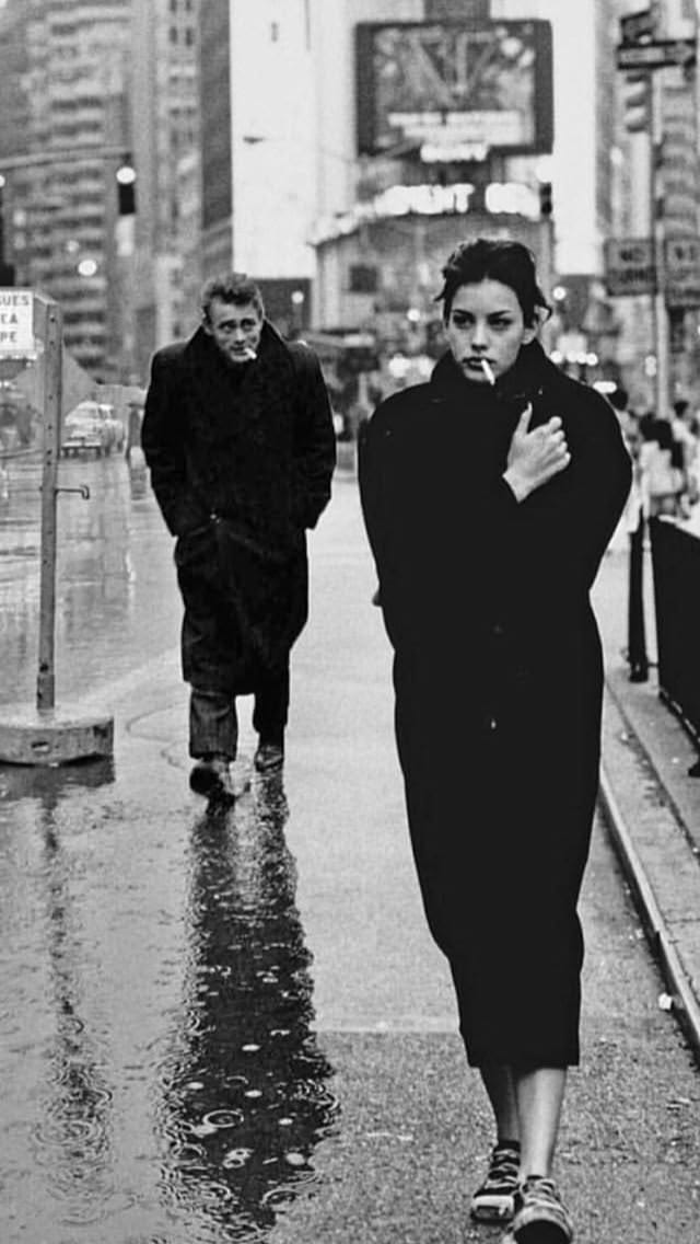 This may contain: two people walking down the street in the rain