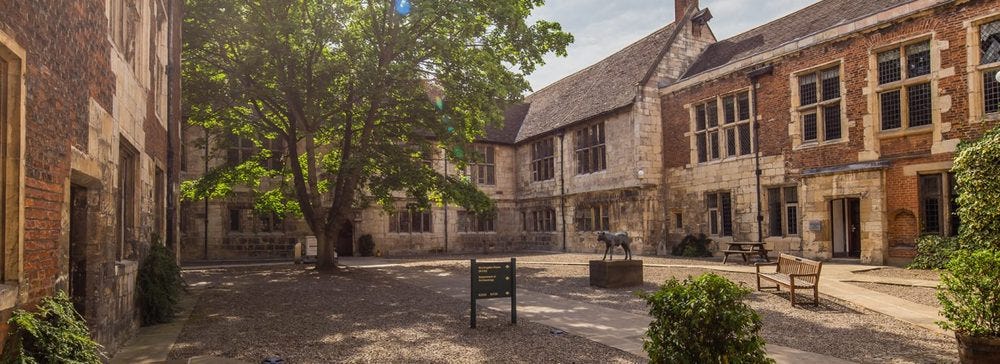 An image of the inner courtyard at King's Manor, York, all gorgeous pale brown stonework surrounding trees.