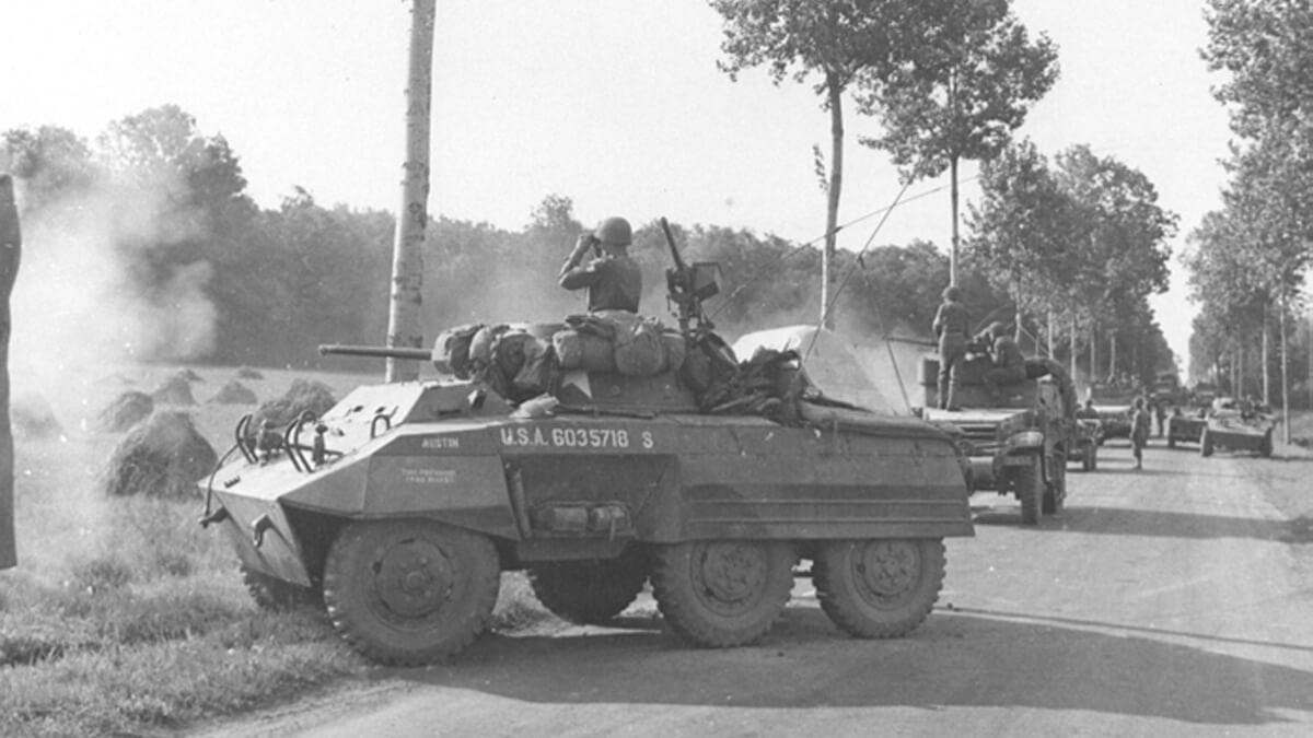 Soldiers in a column of armored vehicles stopped on a road to observe a field.