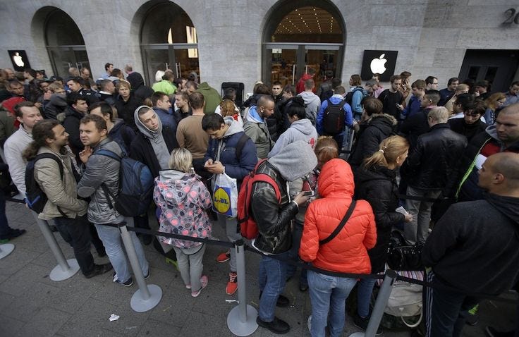 This may contain: a large group of people waiting in line at an apple store for their iphones