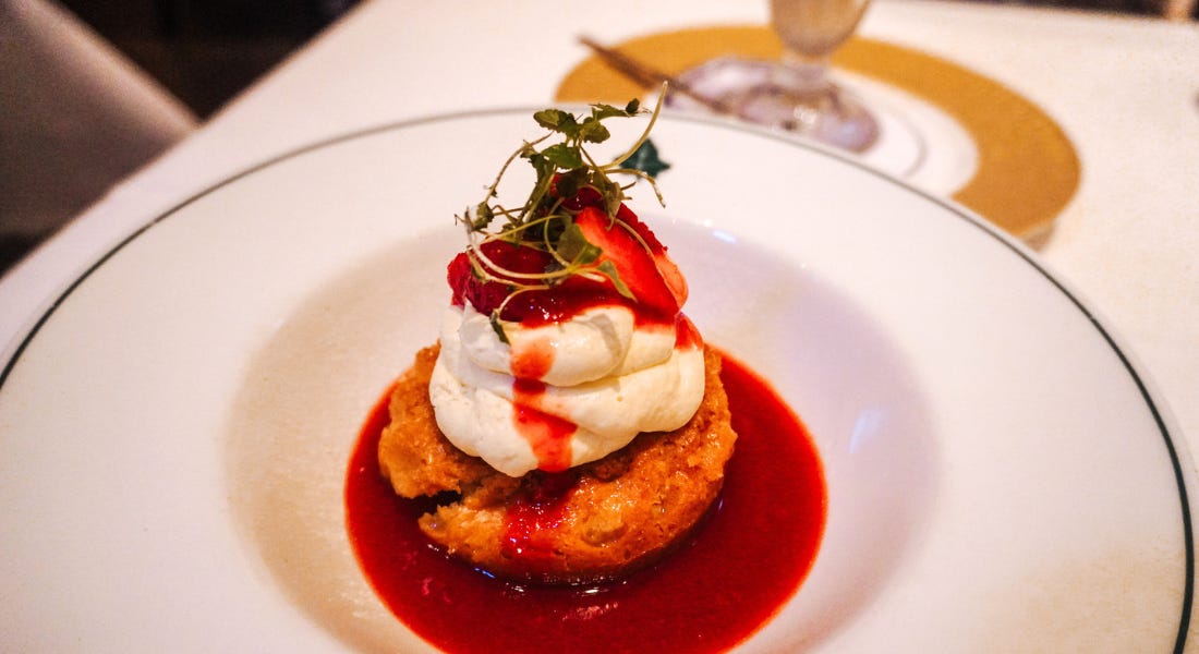 A plate with a dessert with cake, strawberry sauce, and cream, on top of a white tablecloth A plate with a dessert with cake, strawberry sauce, and cream, on top of a white tablecloth