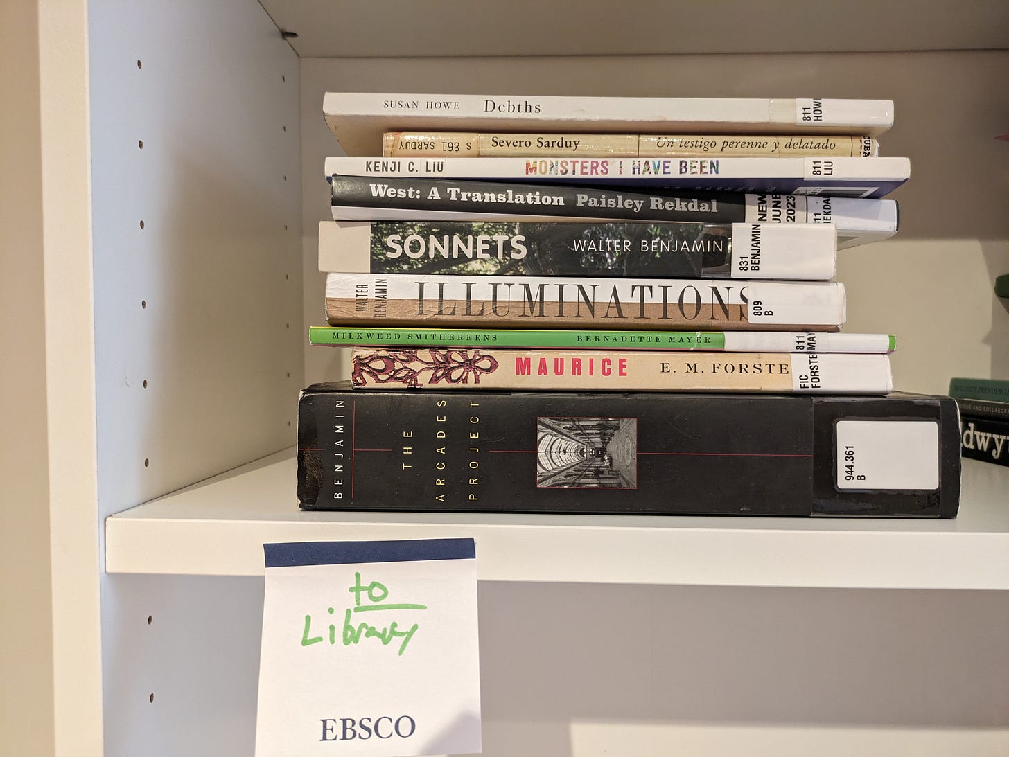 Susan Howe's Debths, Severo Sarduy's Un testigo perenne y delatado, Kenji C. Liu’s Monsters I Have Been, Paisley Rekdal's West: A Translation, Walter Benjamin's Sonnets, Benjamin's Illuminations, Bernadette Mayer's Milkweed Smithereens, E.M. Forster's Maurice, Benjamin's The Arcade Project: a stack of these library books on a white shelf with an EBSCO post-it below saying "To Library" in green Sharpie