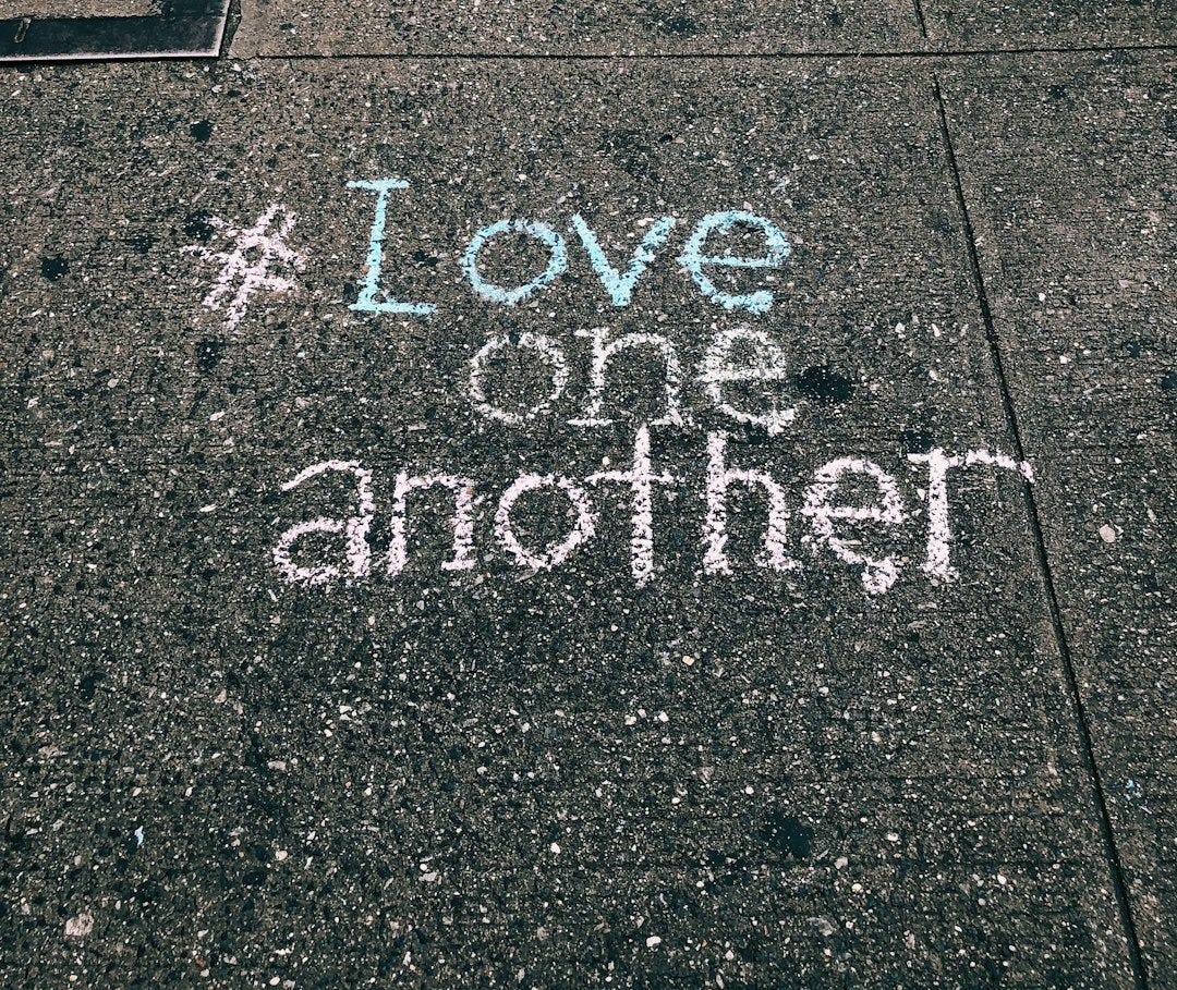 love one another chalk written on concrete floor