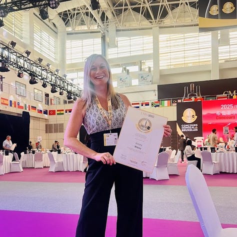 Kristy posing with Concours Mondial de Bruxelles signage across three years of judging: the 2026 Yerevan, Armenia session with the Vine & Wine Foundation of Armenia logo, the 2024 Guanajuato, Mexico session holding a U.S. flag, and the 2025 China session holding her certificate of participation amid rows of judging tables