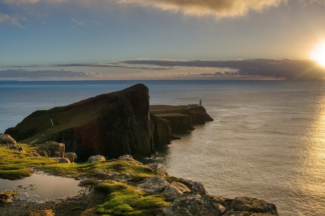 Sunset view over thin rocky peninsula with a lighthouse at its tip