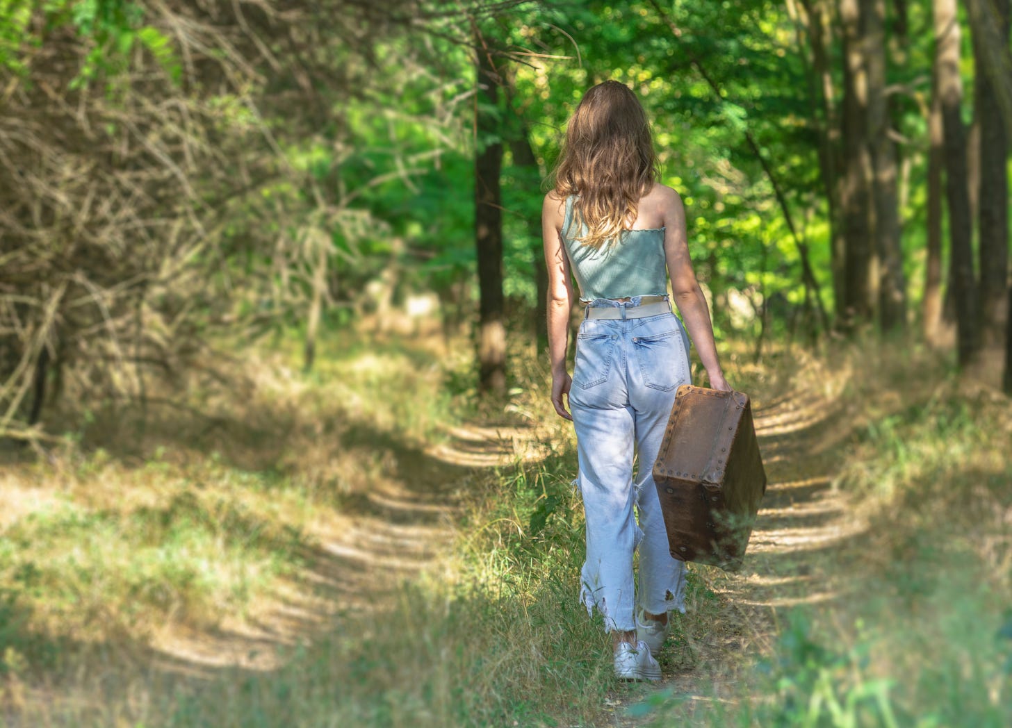 Teen girl carrying a suitcase down a forest path, representing a child’s transition and the parent-child separation that comes with growing up.