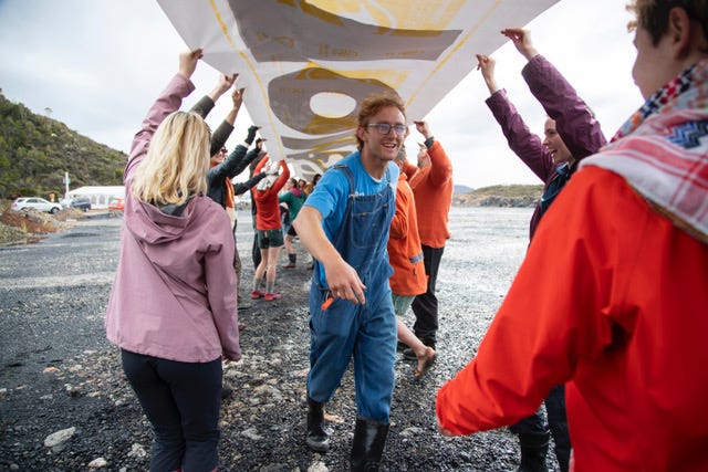 Adam Currie under a large banner during a protest at the mine site on the Denniston Plateau, Easter 2025.