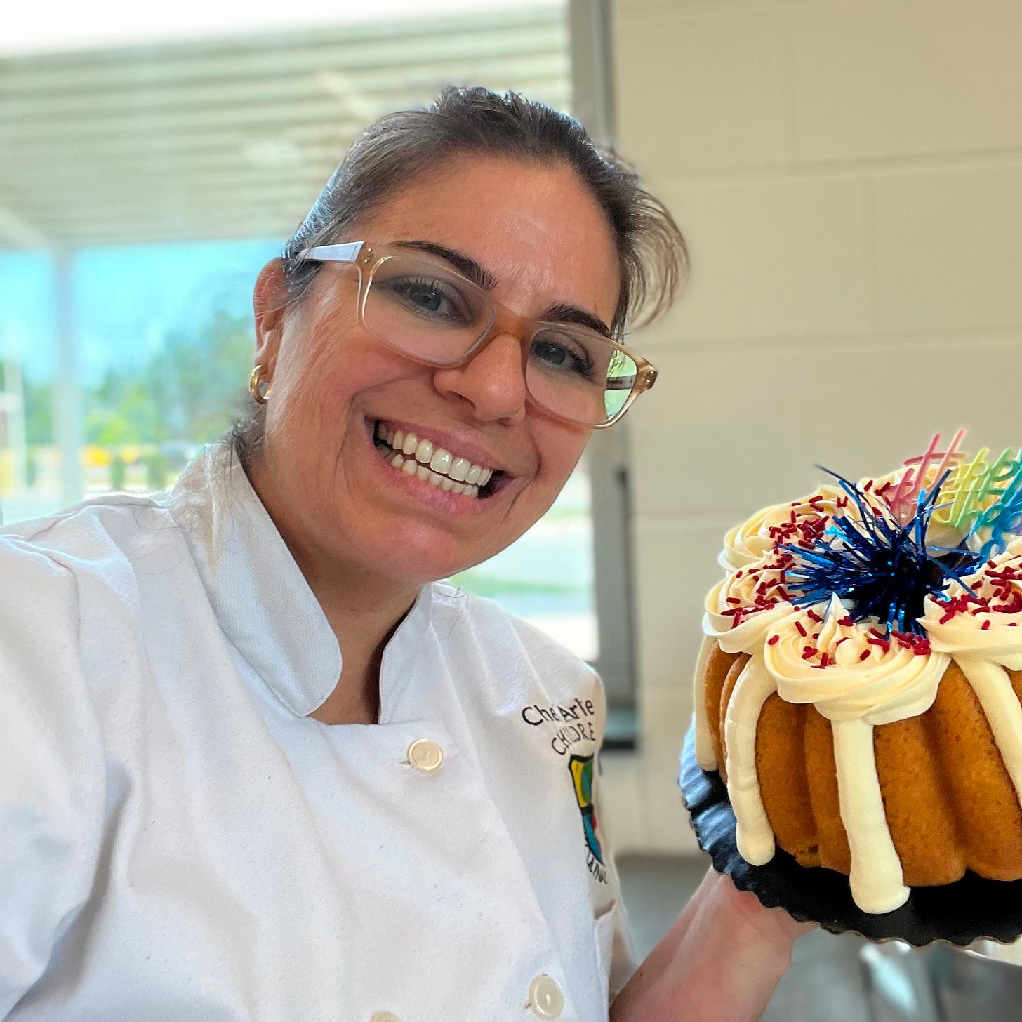 smiling chef in white coat holding a holiday bunt cake