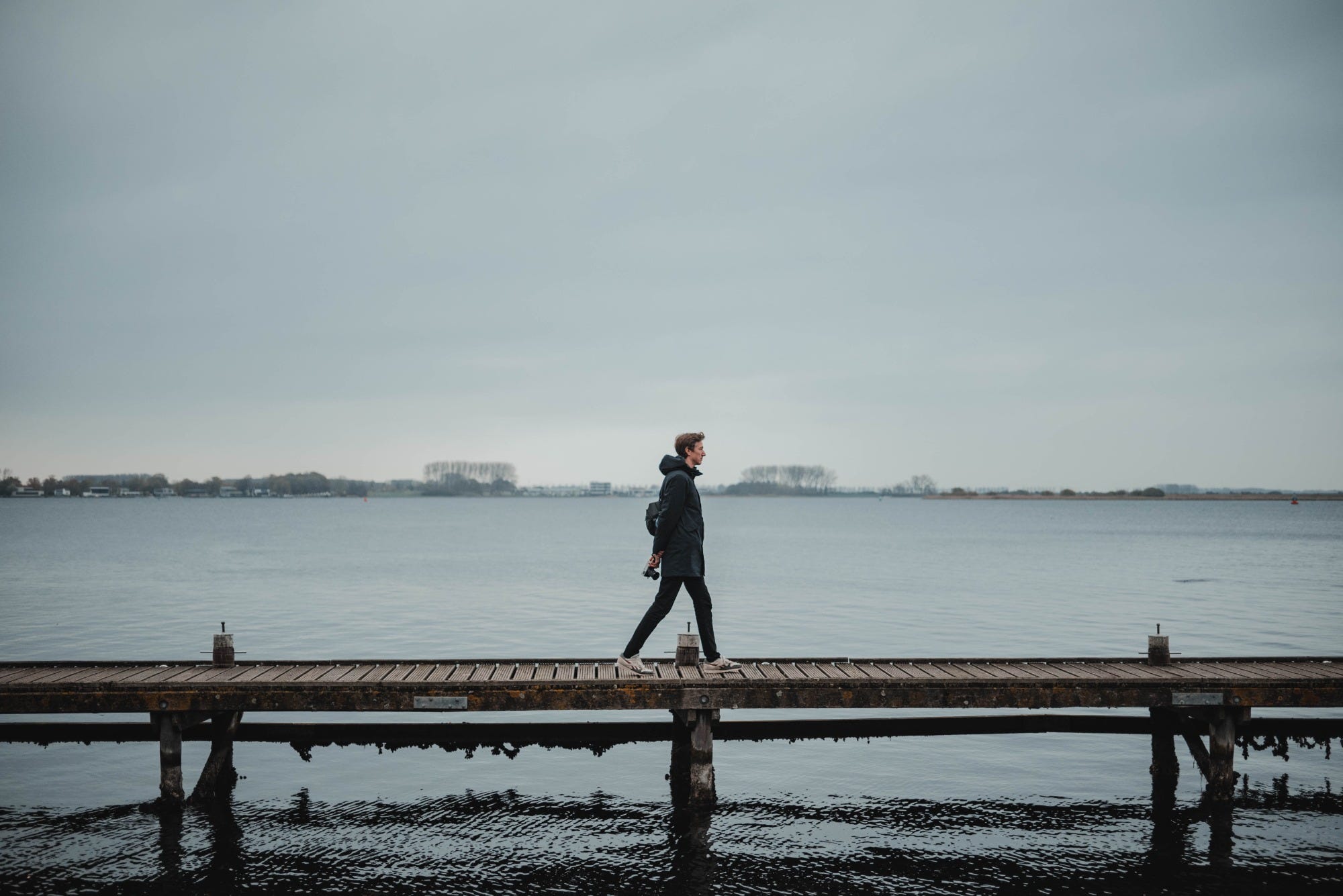 een man loopt over een houten vlonder aan het water