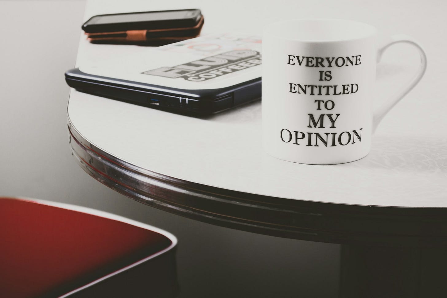 A coffee cup labeled "Everyone is entitled to my opinion", sitting on a desk with a laptop and phone. A coffee cup labeled "Everyone is entitled to my opinion", sitting on a desk with a laptop and phone.