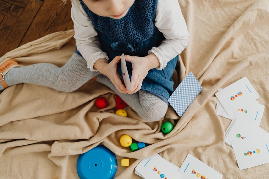 Free A young girl engaged with colorful educational flash cards and toys on a mat indoors. Stock Photo
