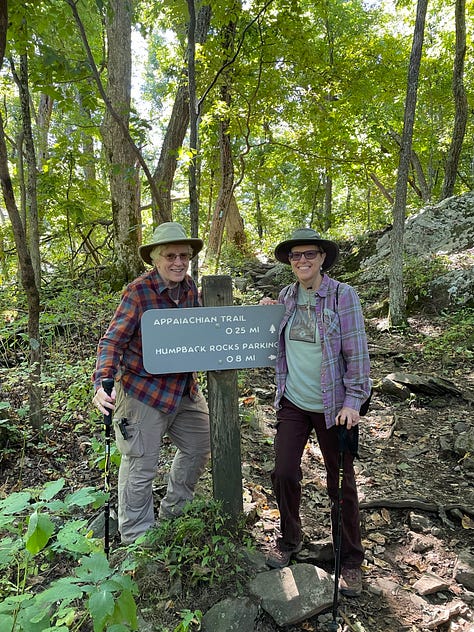 girl and dad with backpacks on in front of stream, two women by trailhead sign in forest, solo woman beside mossy trail