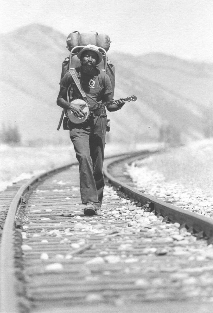 A man walking on train tracks and playing a banjo A man walking on train tracks and playing a banjo